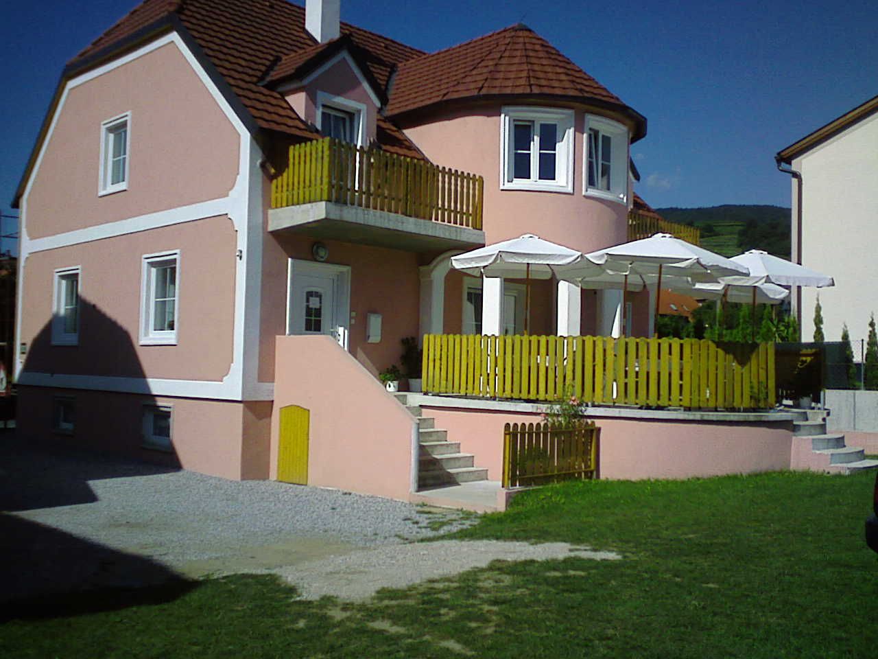 Ein rosa Gästehaus mit Terrasse und Sonnenschirmen.