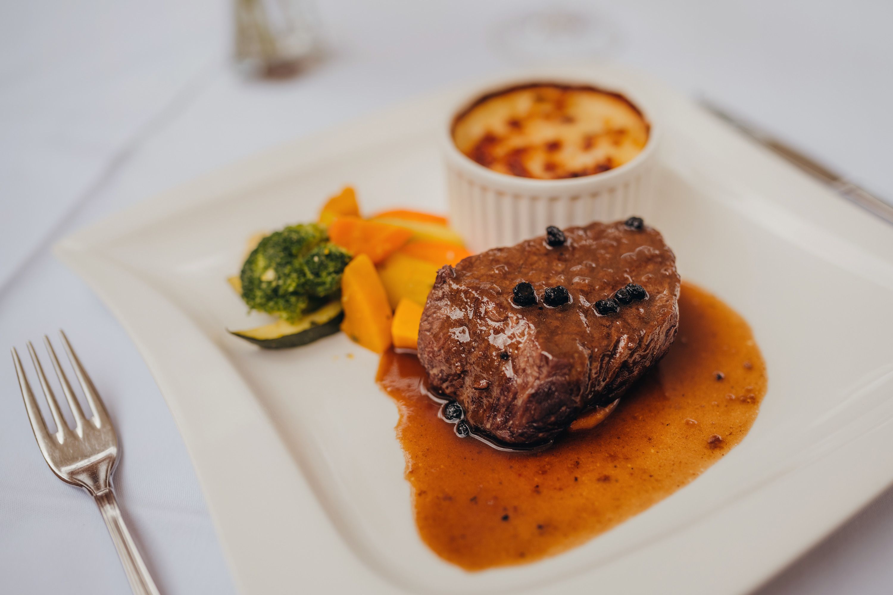 Ein Pfeffersteak mit Sauce, Gemüse und Kartoffelgratin auf einem weißen Teller.