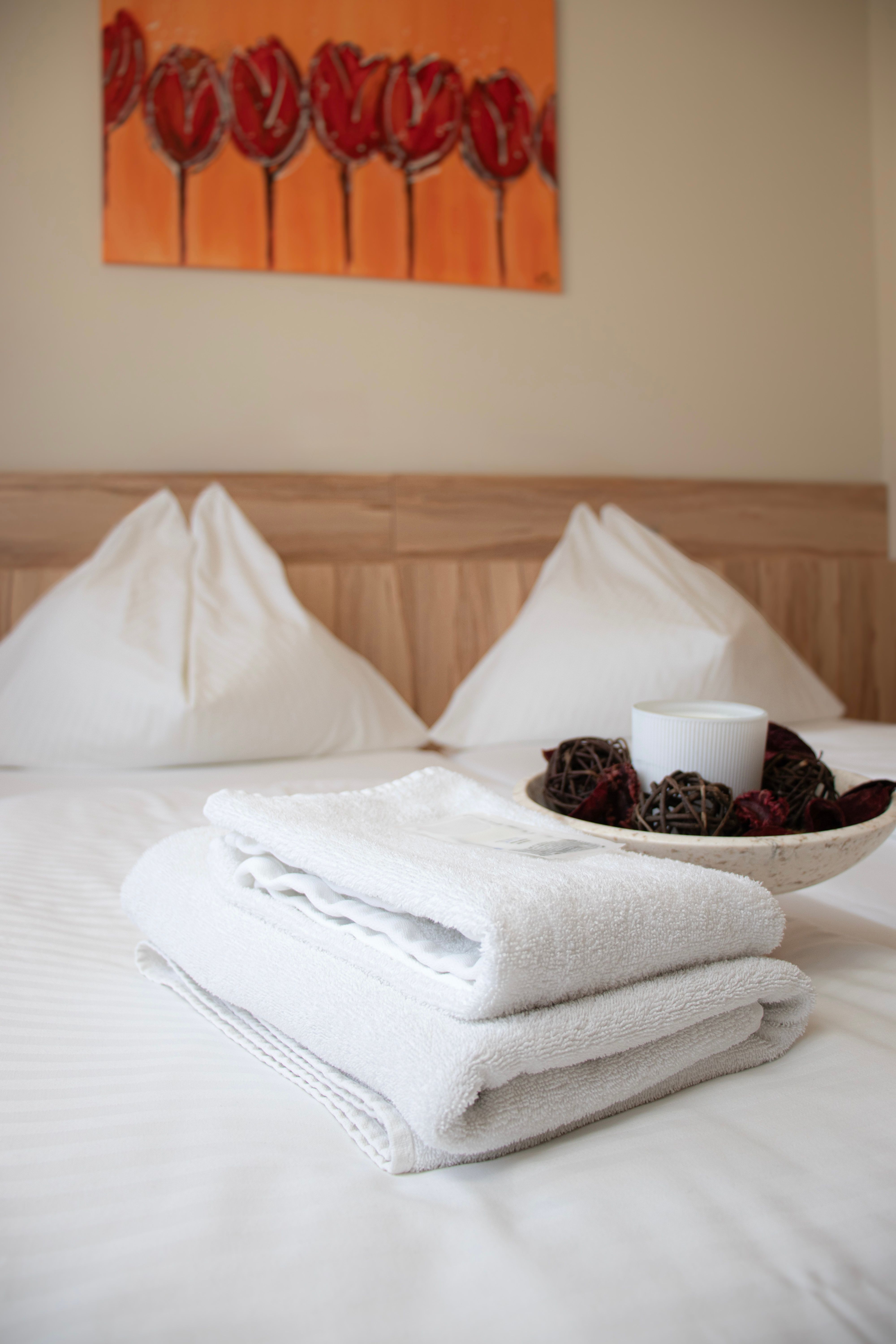 Hotelzimmer im Kolpinghaus mit frisch gemachtem Bett, weißen Handtüchern und dekorativer Schale auf dem Bett.