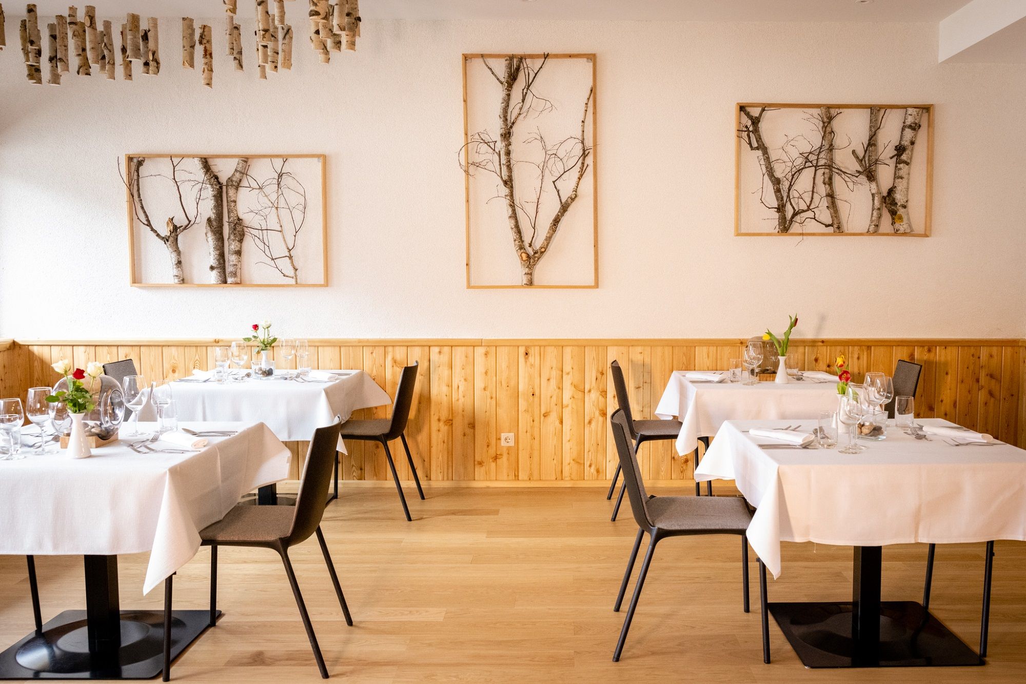 Elegantes Restaurant mit Holzwänden, weißen Tischdecken und Birkenkunst an den Wänden.