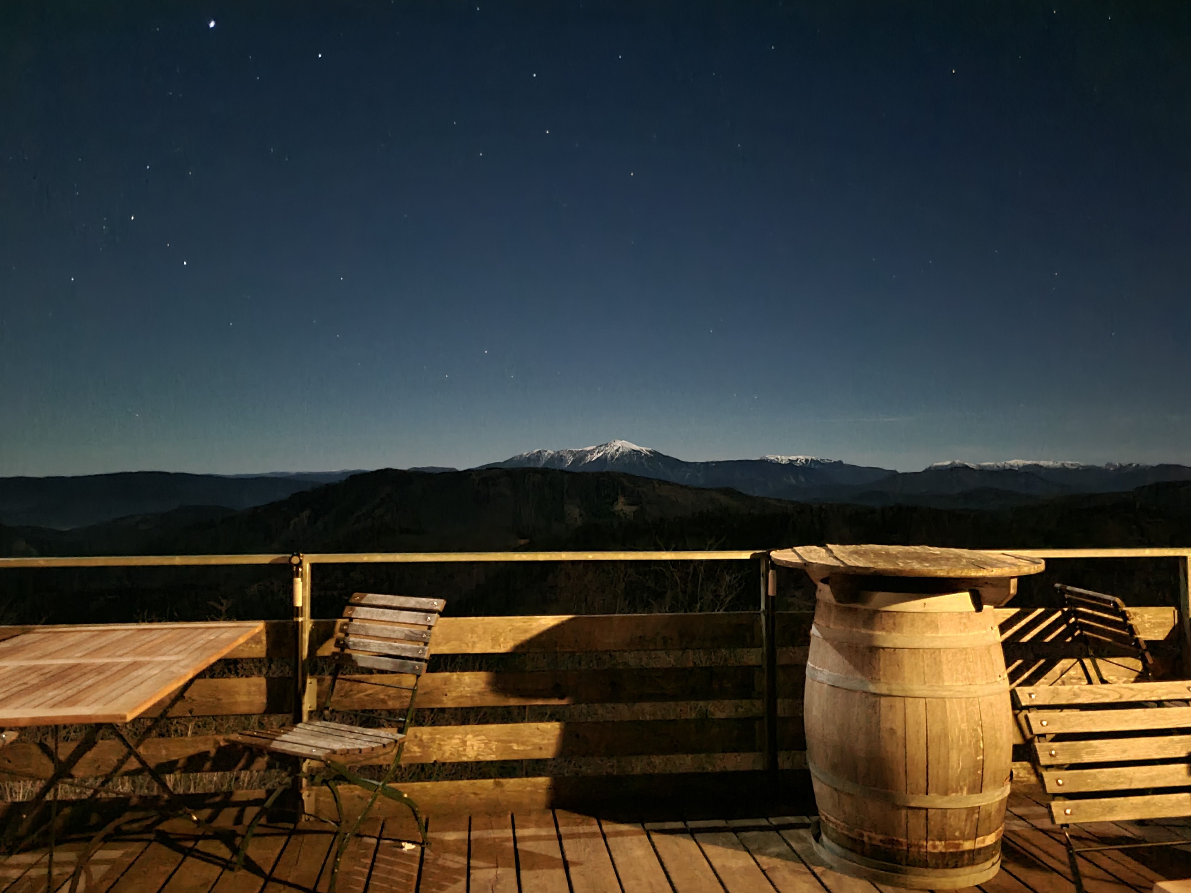 Nachtaufnahme von der Enzianhütte3 mit Sternenhimmel, Terrasse, Tisch, Stühlen und Blick auf schneebedeckte Berge.