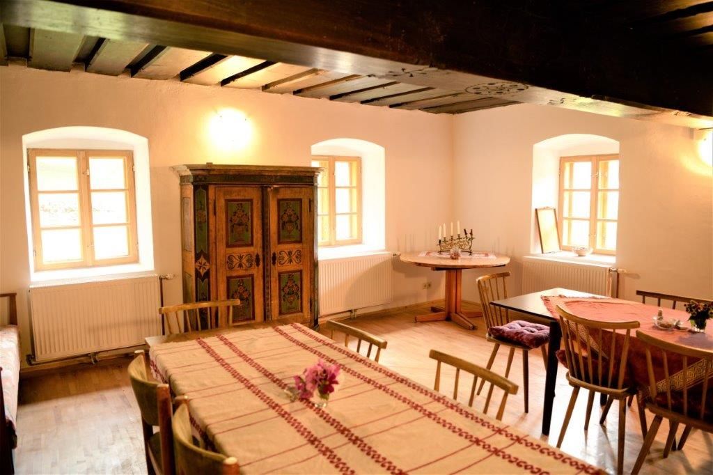 Gemütliche Stube mit Holzmöbeln, Tischdecken und einem bemalten Schrank.