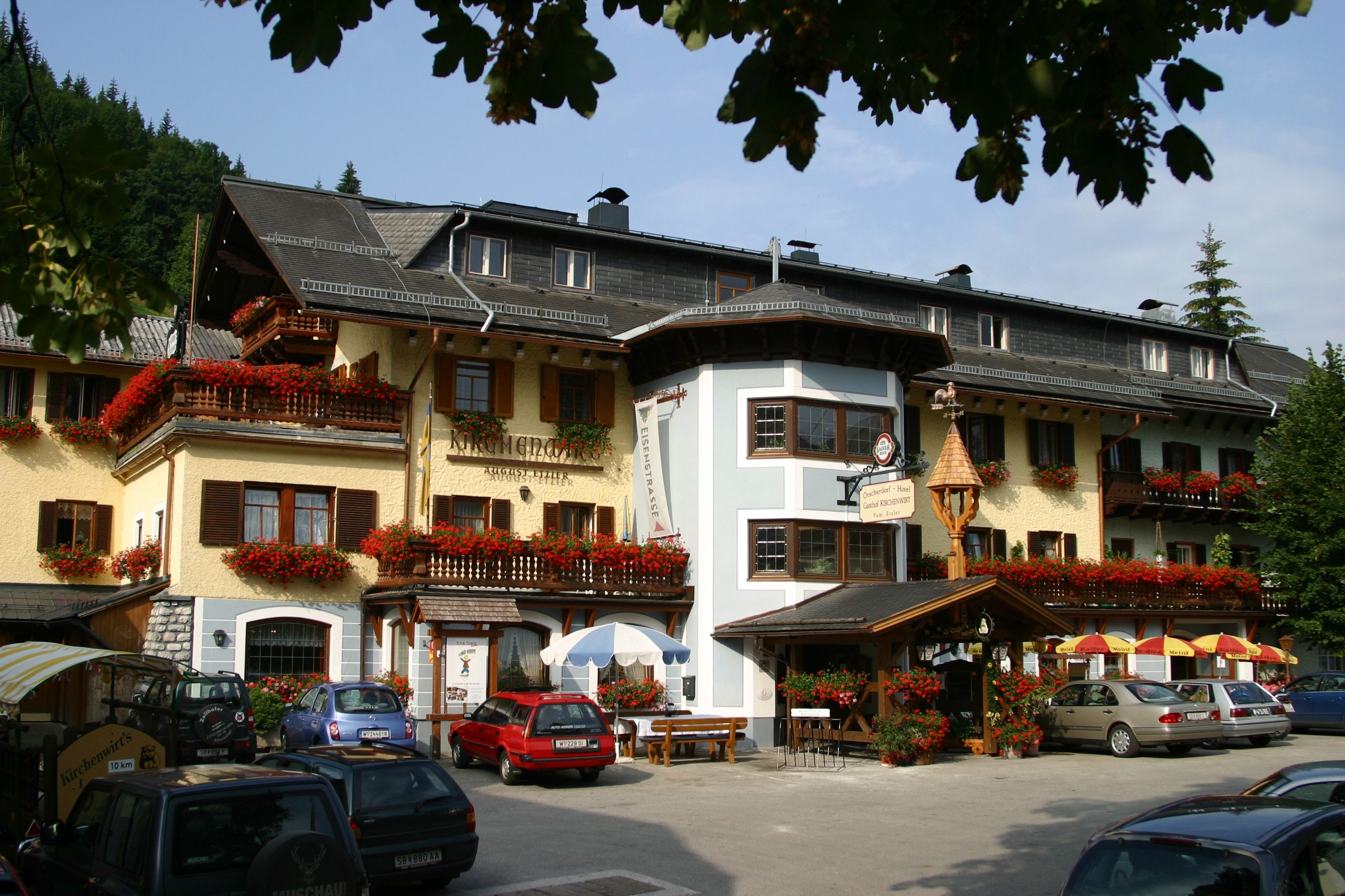 Ein traditionelles Gasthaus mit blumengeschmückten Balkonen und geparkten Autos davor.