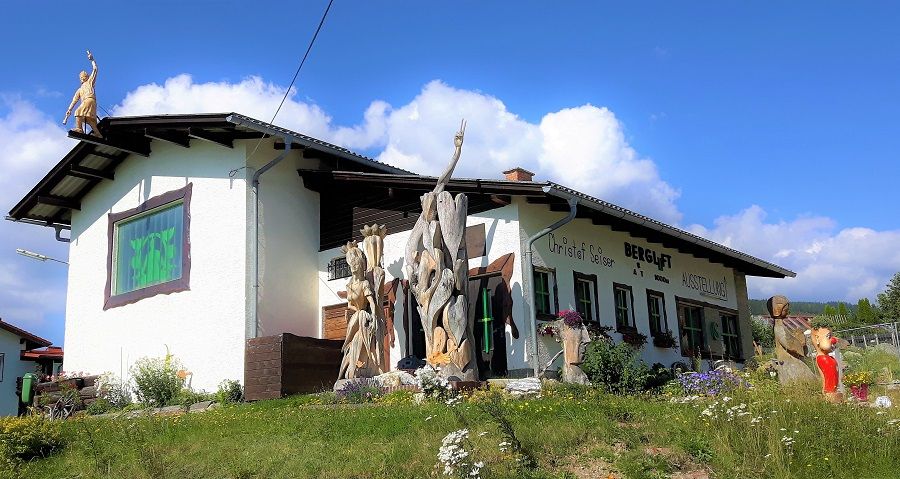 Ein Gebäude mit der Aufschrift 'Bergluft' und Holzskulpturen im Vordergrund.