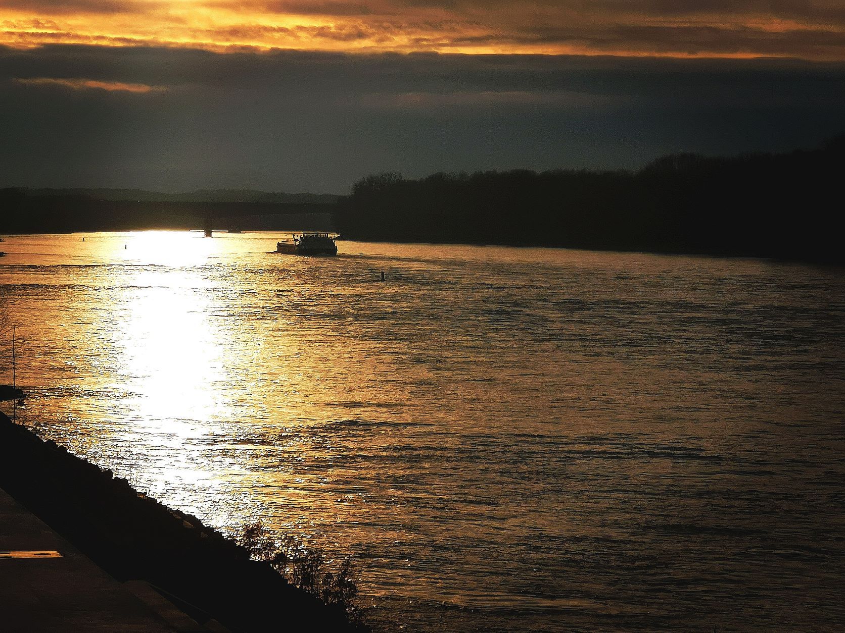 Sonnenuntergang über einem Fluss mit einem Boot und dunklen Wolken am Himmel.