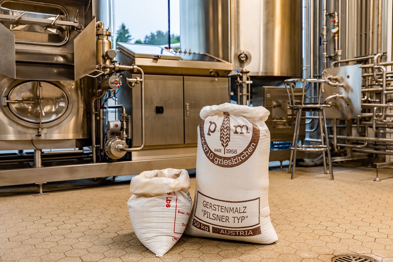 Säcke mit Gerstenmalz in einer Brauerei vor Edelstahlmaschinen.