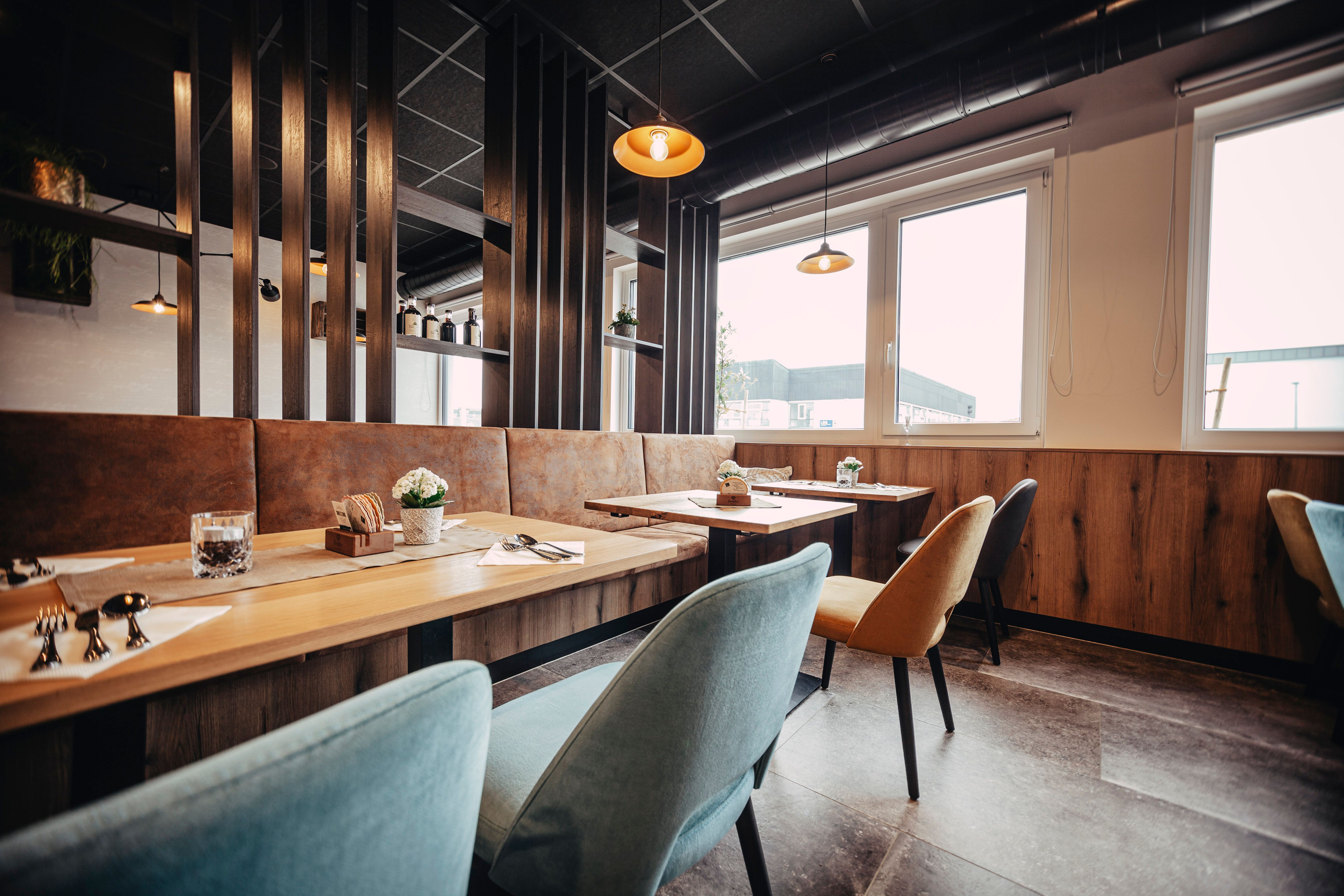 Modern eingerichtetes Restaurant mit Holztischen, bunten Stühlen und großen Fenstern.