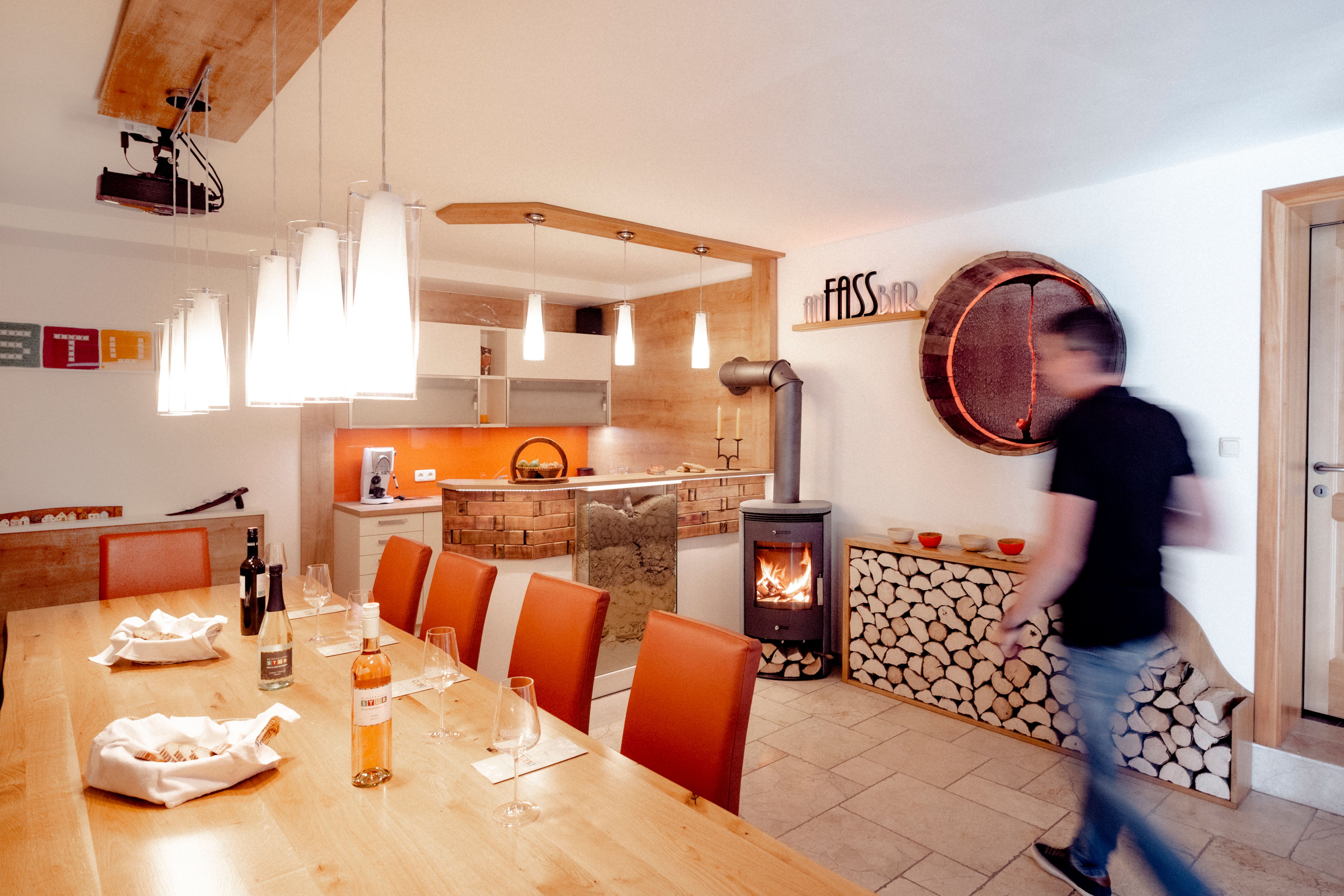 Ein Verkostungsraum mit Holztisch, Weingläsern, Kamin und moderner Beleuchtung.