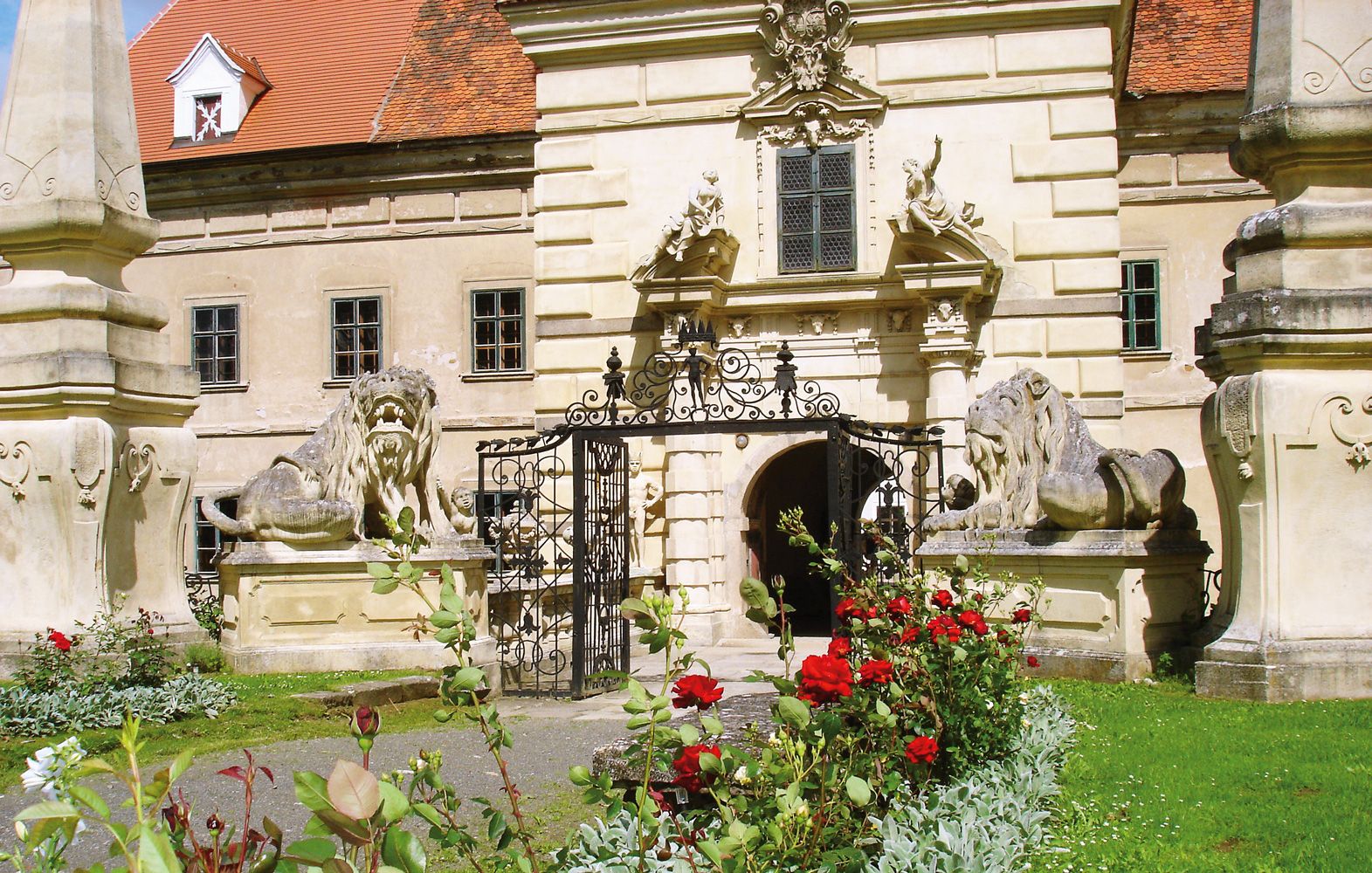 Eingang von Schloss Greillenstein mit Löwenstatuen und blühenden Rosen im Vordergrund.