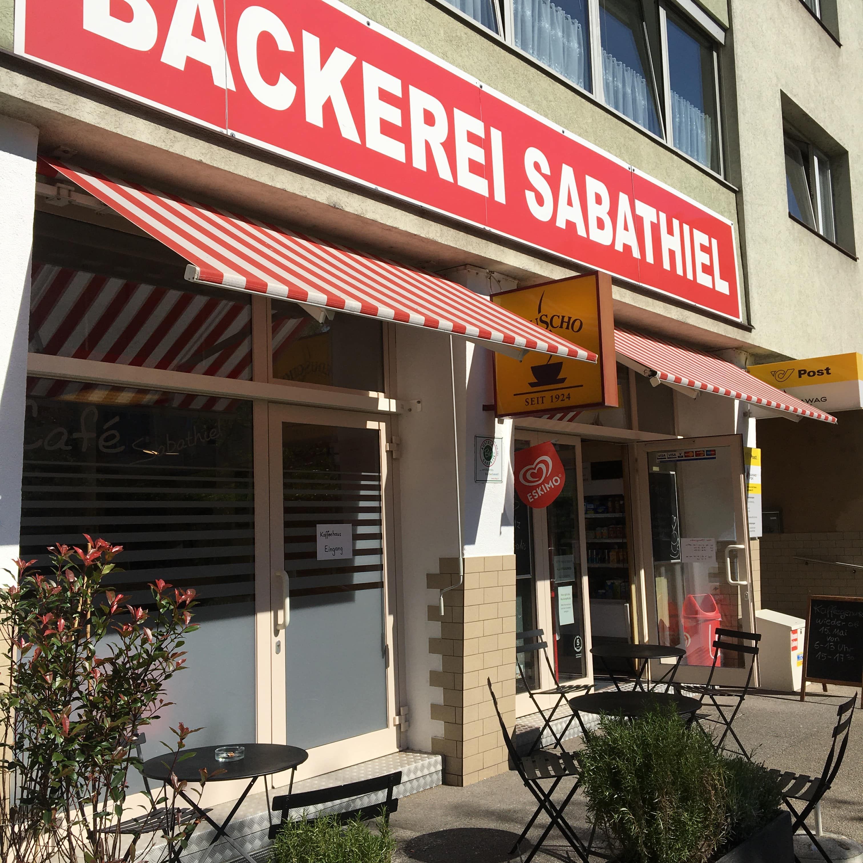 Außenansicht einer Bäckerei mit roten Markisen und Sitzgelegenheiten im Freien.