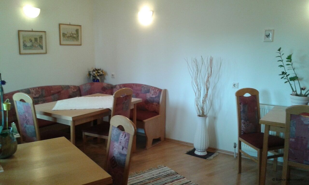 Gemütliche Sitzecke in einer Gemeinschaftsküche mit Holztischen und gepolsterten Stühlen.