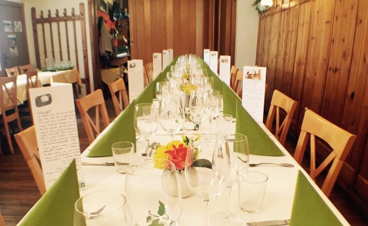 Langer, festlich gedeckter Tisch in einer rustikalen Gaststube mit Holzw&auml;nden und Dekoration.