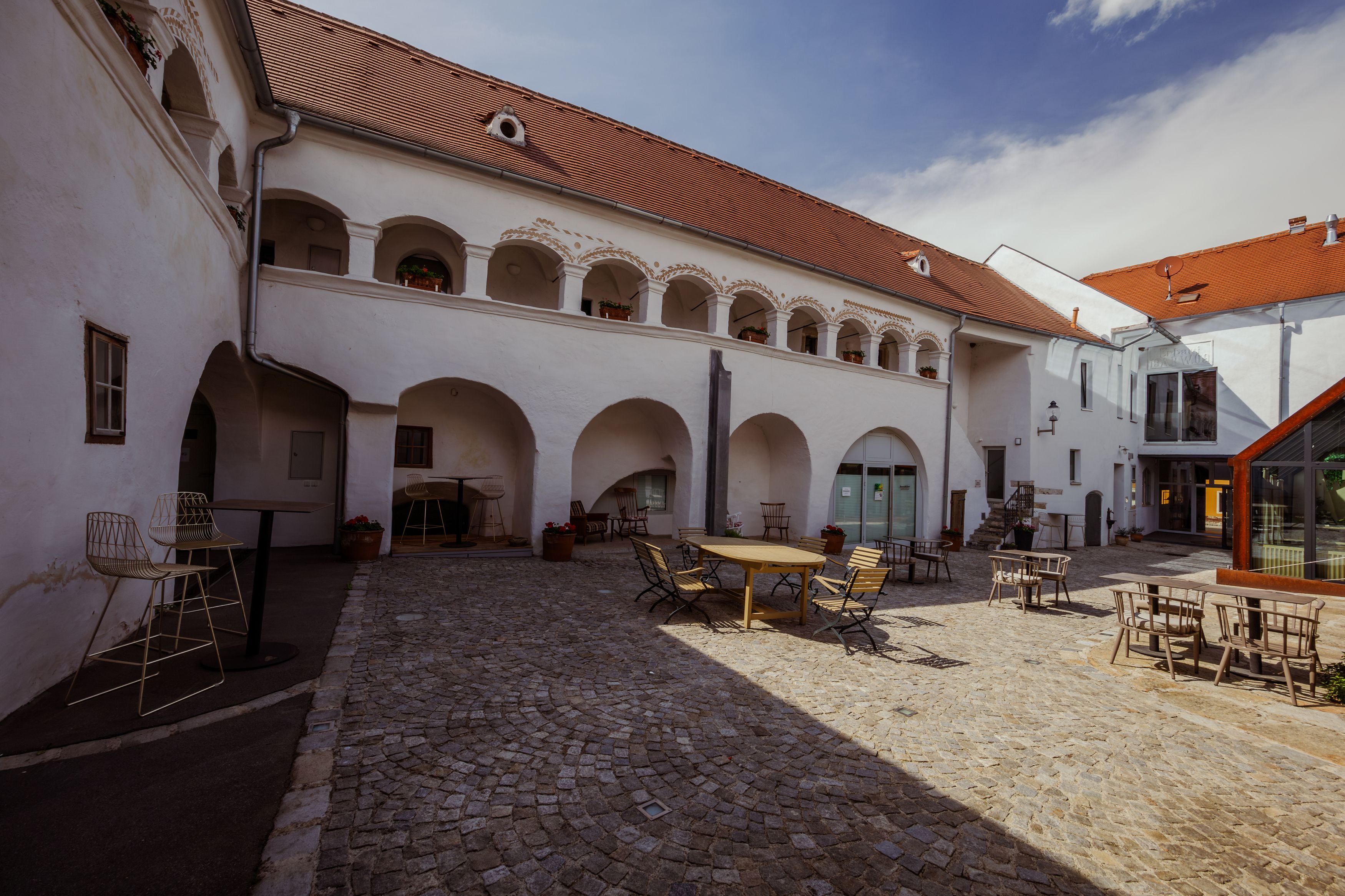 Innenhof eines historischen Gebäudes mit Arkaden und Sitzgelegenheiten.