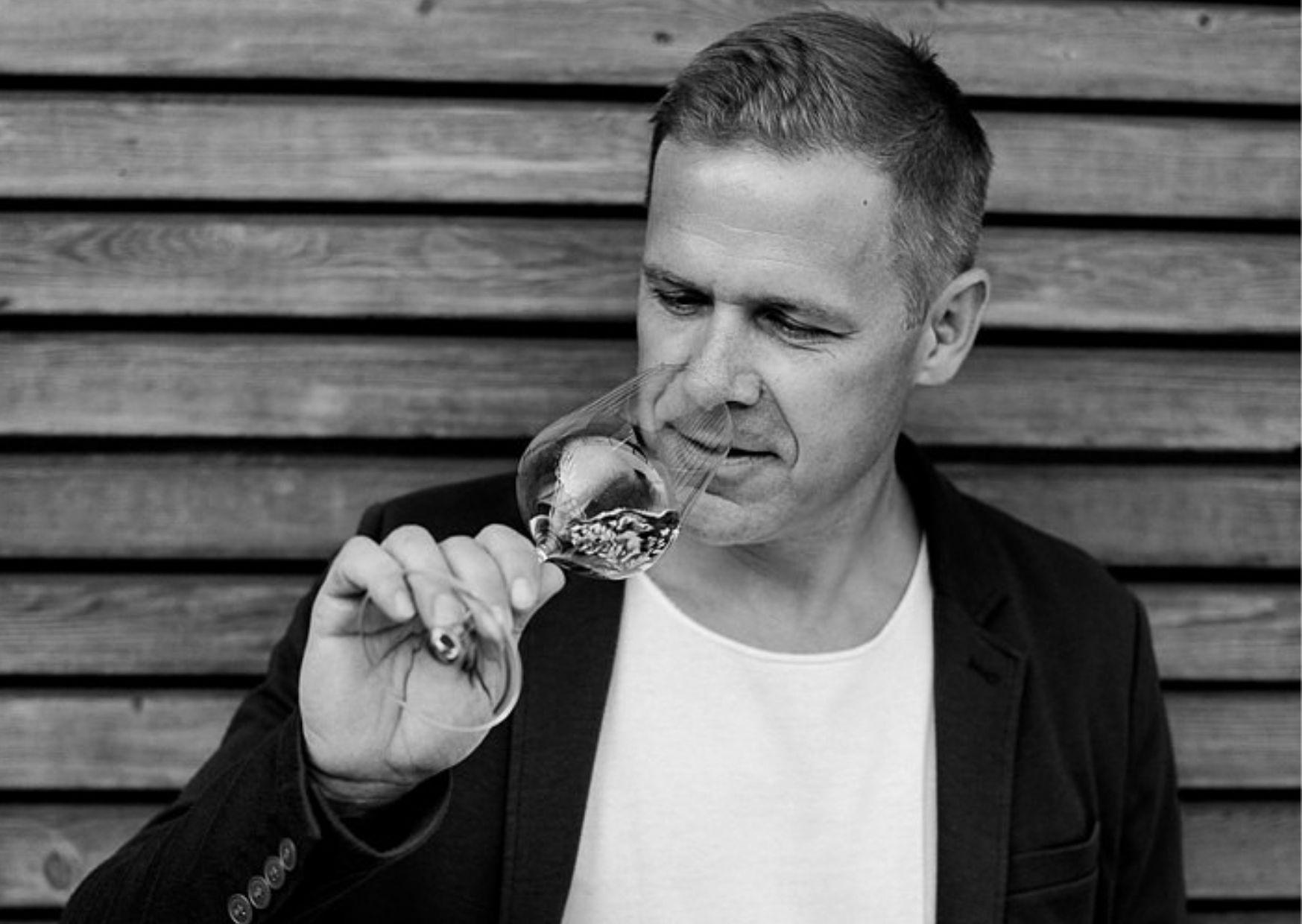 Ein Mann riecht an einem Weinglas vor einer Holzwand.