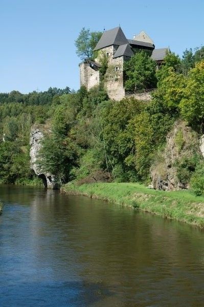 Burg auf einem bewaldeten Hügel am Flussufer.