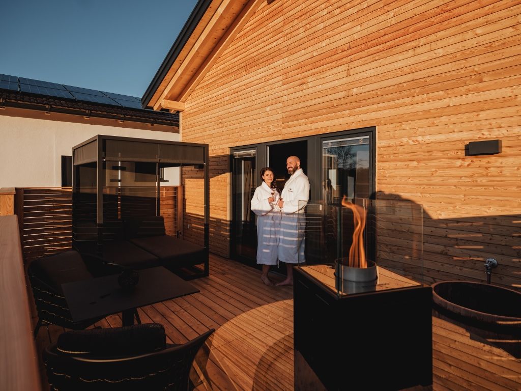 Terrasse mit Himmelbett, Feuerstelle und zwei Personen in Bademänteln.
