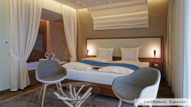 Doppelzimmer, © Familie Würtl Modernes Doppelzimmer mit großem Bett, zwei grauen Stühlen und einem Glastisch.