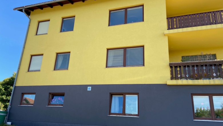 Anke´s Ferienwohnung, © Wiener Alpen Gelbes Gebäude mit braunen Fenstern und Balkonen, blauer Himmel im Hintergrund.