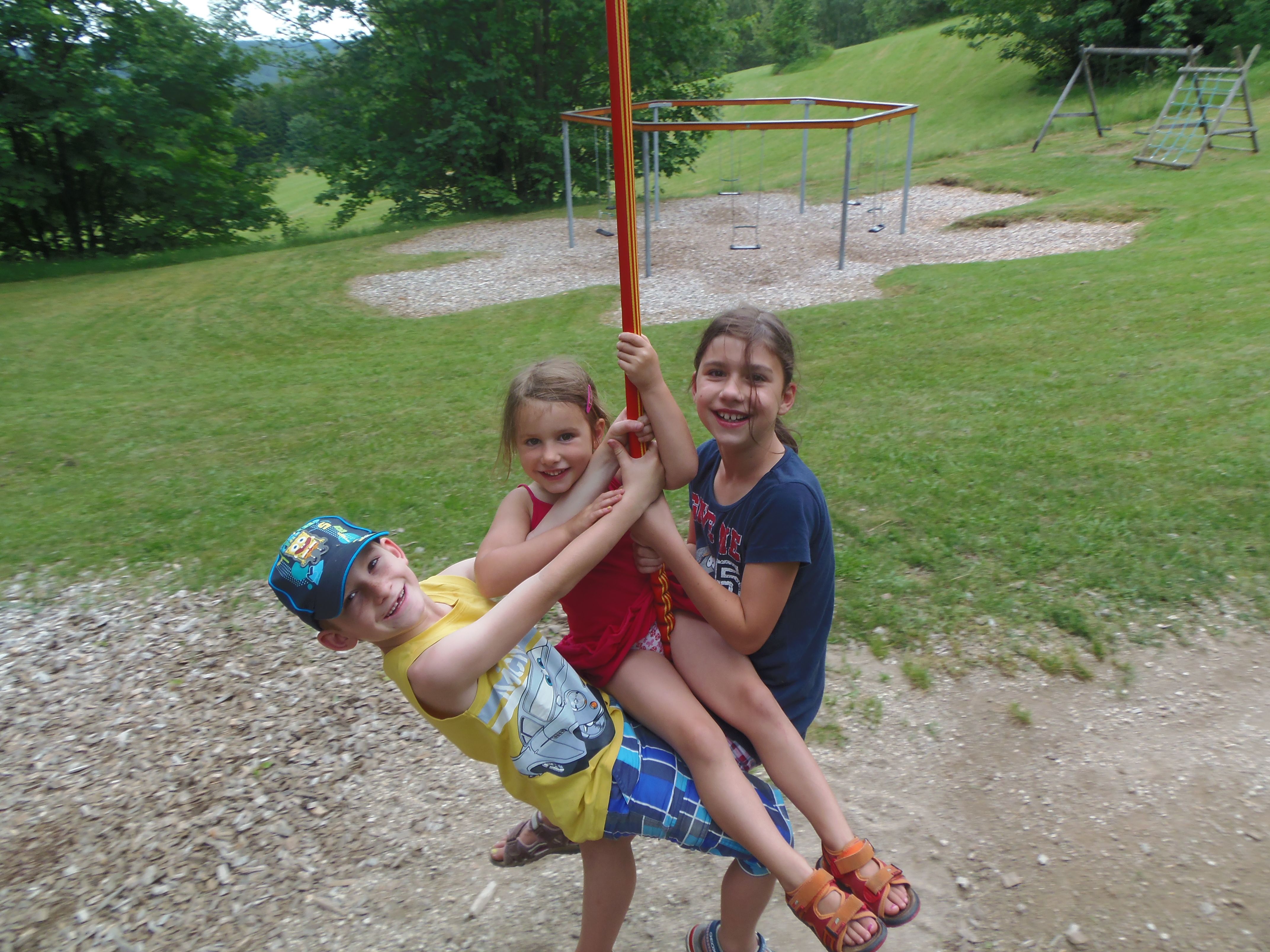 Drei Kinder schaukeln fröhlich an einer Seilbahn auf einem Spielplatz.