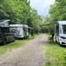 Zwei Wohnmobile und ein Van auf einem Campingplatz im Gr&uuml;nen mit ausgebreiteten Markisen und Campingst&uuml;hlen.