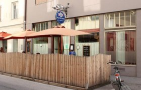 Außenansicht eines Cafés mit Holzzaun und Sonnenschirmen.