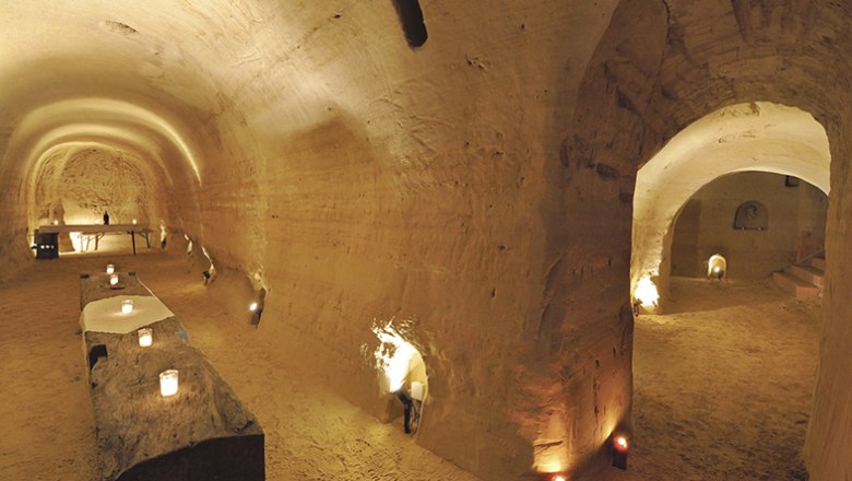 Unterirdischer Sandsteinkeller mit Kerzenlicht und rustikalen Tischen.