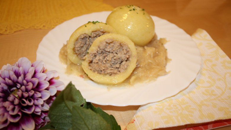 Ein Teller mit Waldviertler Fleischknödeln auf Sauerkraut, dekoriert mit einer Blume.