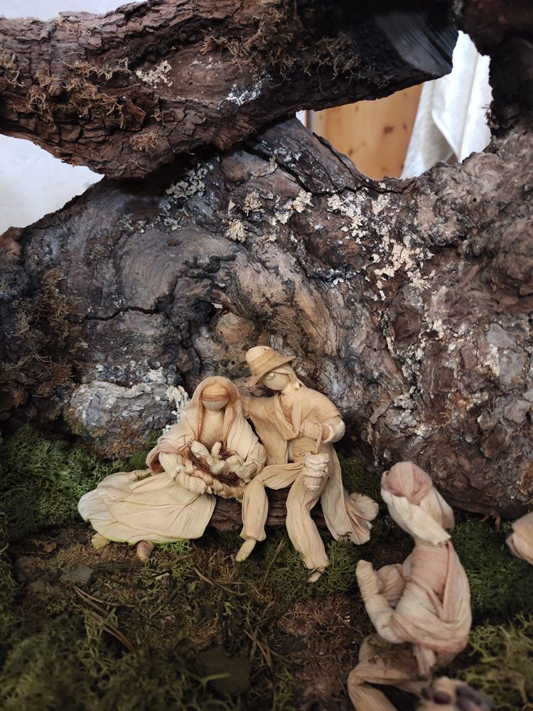 Naturkrippe mit Figuren aus Maisschalen unter einem Baumstamm.