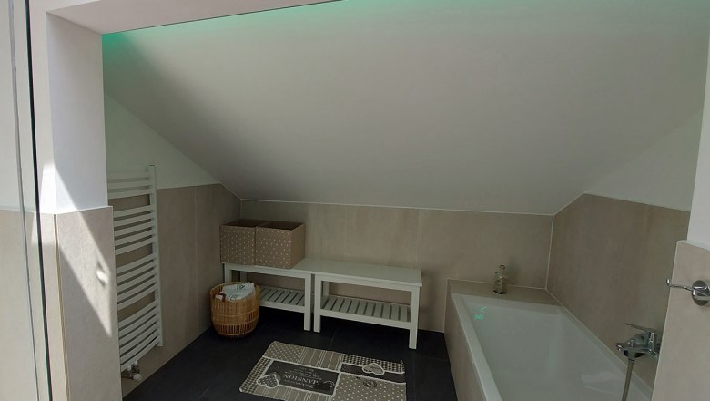 Modernes Badezimmer mit Badewanne, Dachschr&auml;ge, Handtuchhalter und Dekoration.