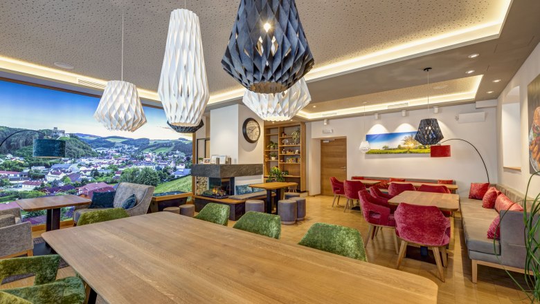 Innenansicht eines modernen Bistros mit Holztischen, bunten St&uuml;hlen und gro&szlig;en, dekorativen Lampen.