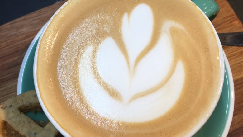 Cappuccino mit Latte Art in einer grünen Tasse auf einem Holzbrett.