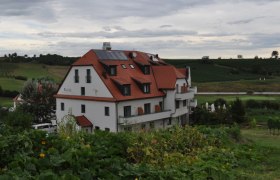 Ein Hotel mit rotem Dach inmitten einer grünen Landschaft mit Weinbergen im Hintergrund.