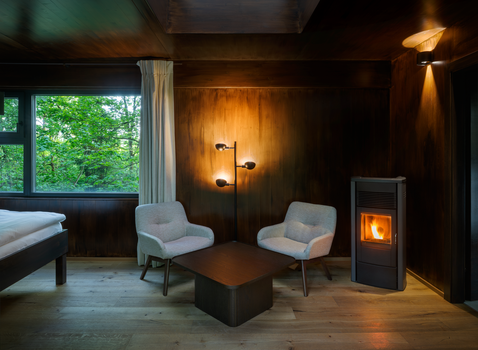 Innenansicht eines gemütlichen Baumhauses mit zwei Sesseln, einem Tisch und einem Kaminofen.