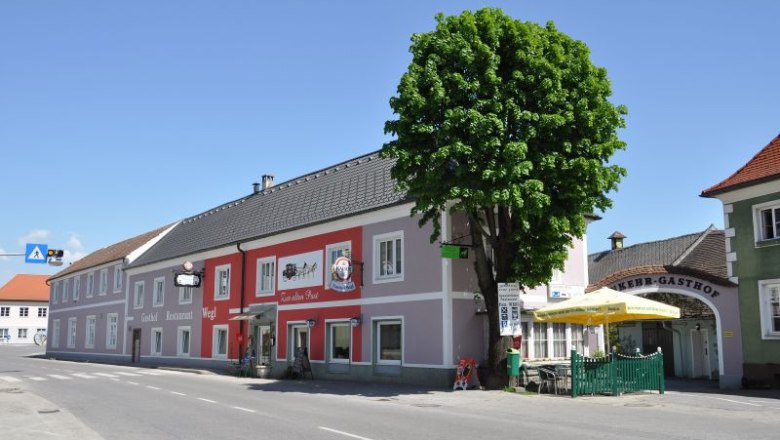 Gasthof Wegl an einer Straße mit Baum und Sonnenschirmen.