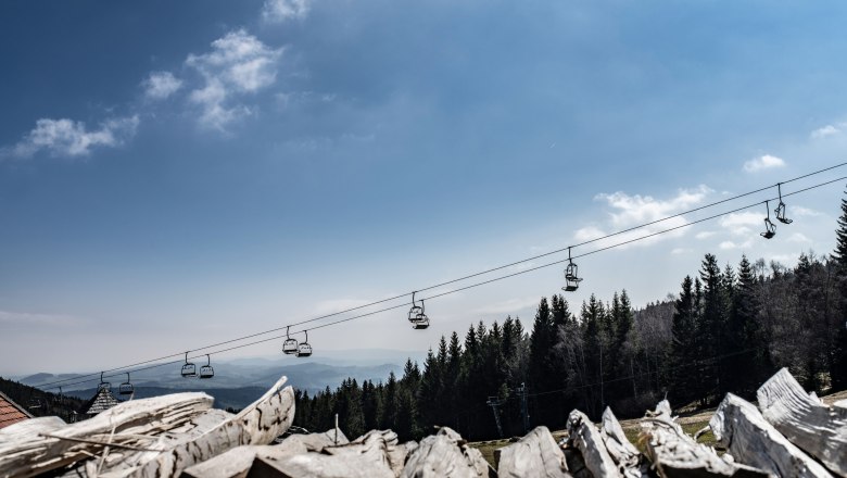 Blick auf eine Seilbahn &uuml;ber einem Wald mit blauem Himmel im Hintergrund.