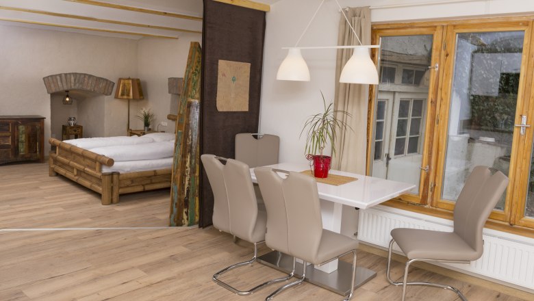 Innenansicht einer Ferienwohnung mit Esstisch, St&uuml;hlen, Bett und Fenster.