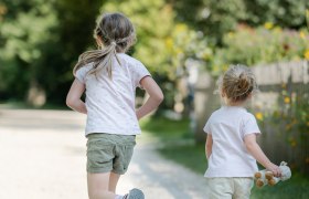 Zwei Kinder laufen auf einem Kiesweg in einem gr&uuml;nen Park.