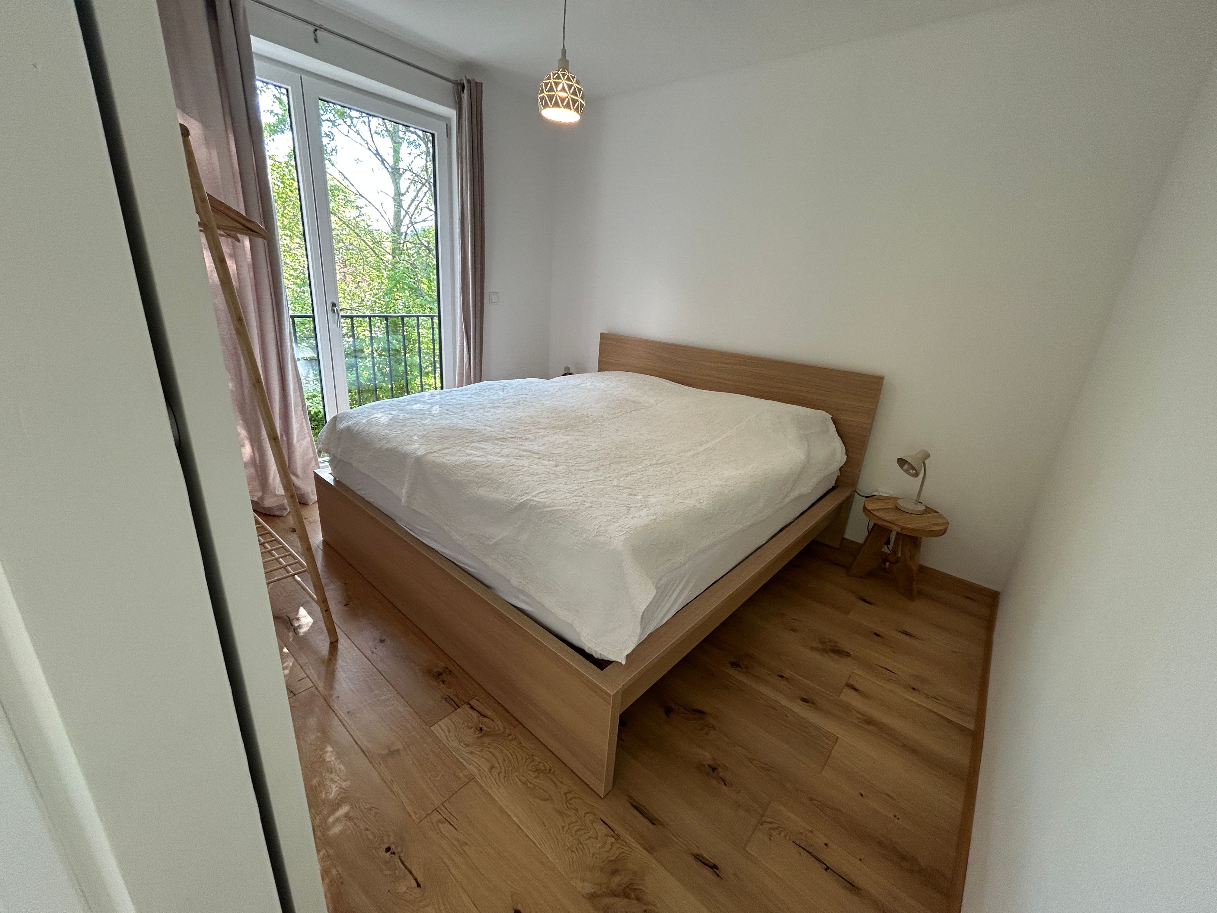 Schlafzimmer mit Holzboden, Doppelbett und Fenster mit Blick ins Grüne.