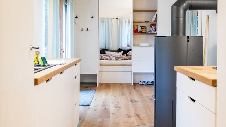 Innenansicht eines modernen, kompakten Wohnraums mit Holzfu&szlig;boden, K&uuml;chenzeile und Schlafbereich.