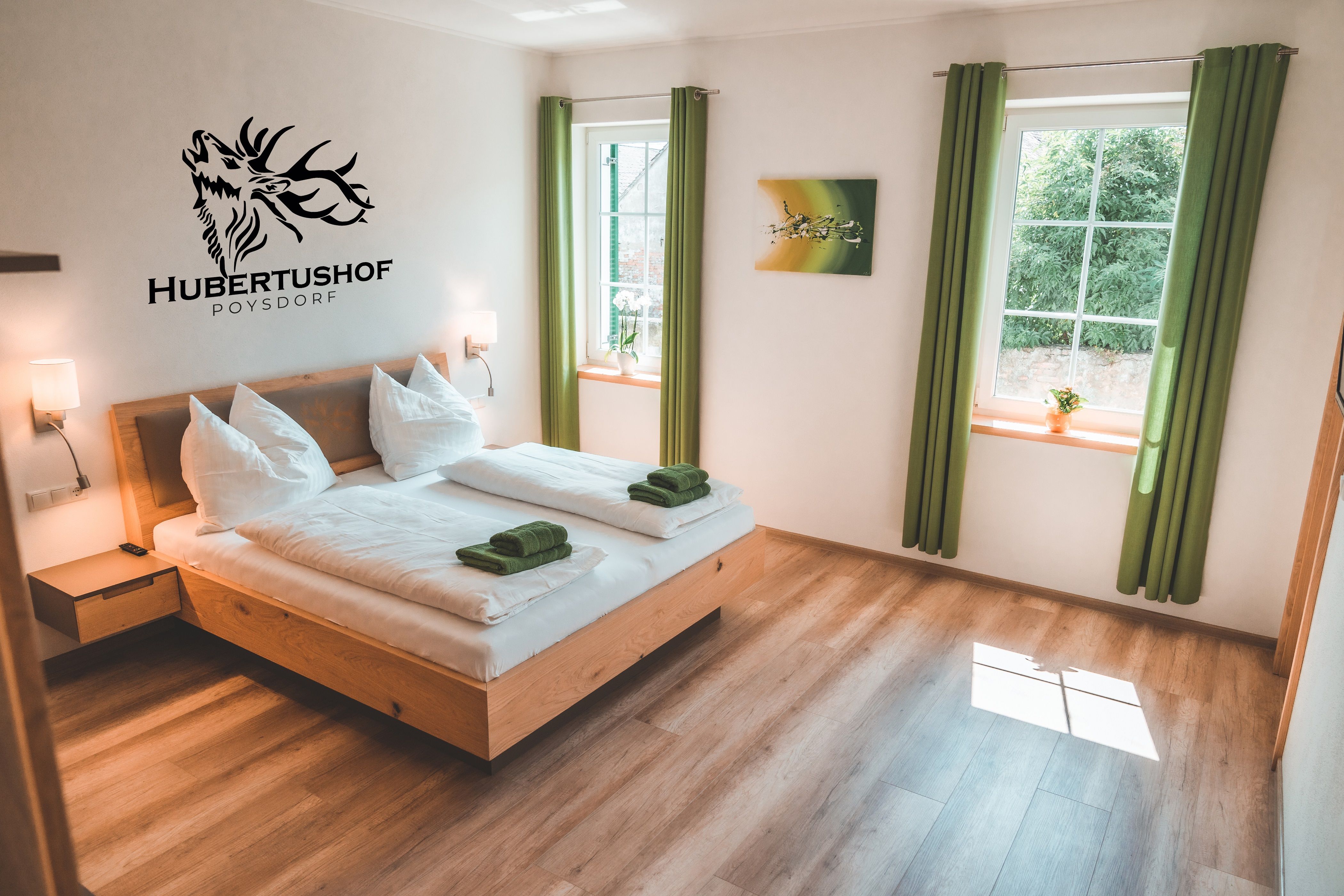 Modernes Gästezimmer mit Doppelbett, grünen Vorhängen und Wanddekoration im Hubertushof Poysdorf.