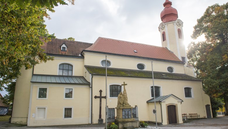 Pfarrkirche Heiligeneich mit Statue und Kreuz im Vordergrund.
