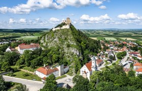 Luftaufnahme einer Burg auf einem H&uuml;gel mit umliegendem Dorf und Feldern.