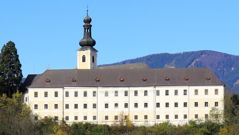 Schloss Gloggnitz vor bewaldeten Hügeln und blauem Himmel.