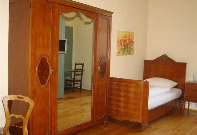 Ein traditionell eingerichtetes Zimmer mit Holzschrank, Einzelbett und Stuhl.
