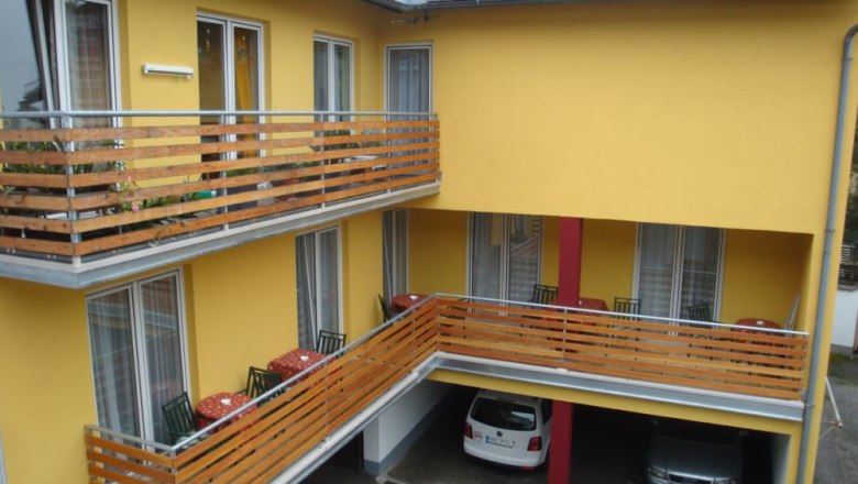 Gelbes Gebäude mit Balkonen und geparkten Autos darunter.