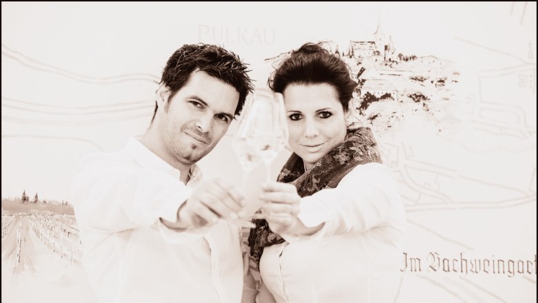 Ein Mann und eine Frau sto&szlig;en mit Weingl&auml;sern an, im Hintergrund eine Zeichnung von Pulkau.