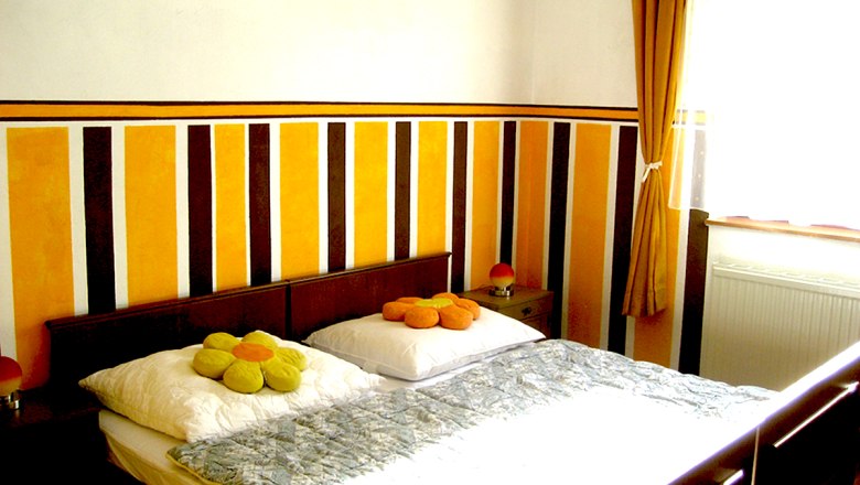 Ein Schlafzimmer mit einem Doppelbett, gestreifter Wand und gelben Vorh&auml;ngen.