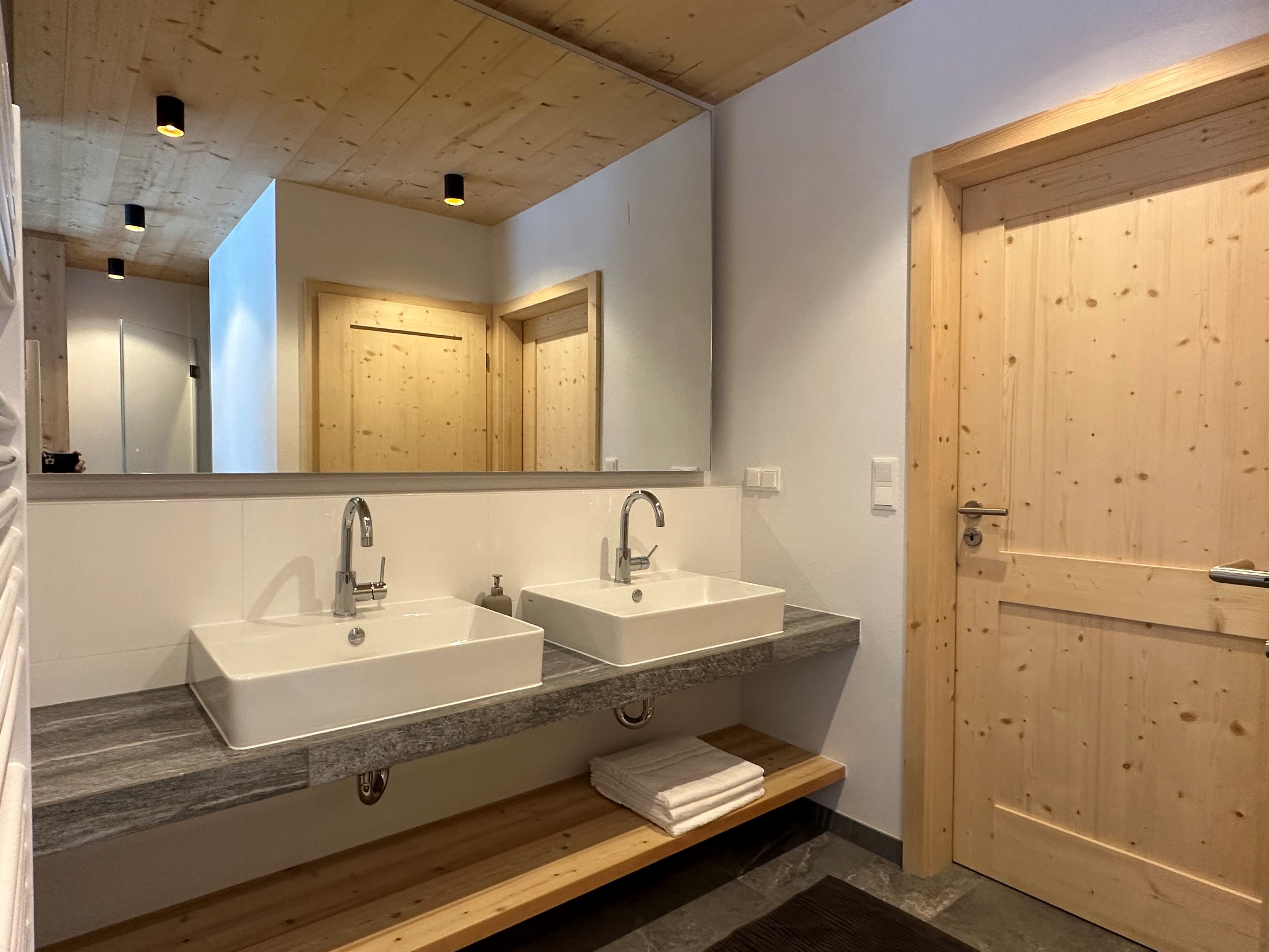 Modernes Badezimmer mit zwei Waschbecken, Holzdecke und -türen.