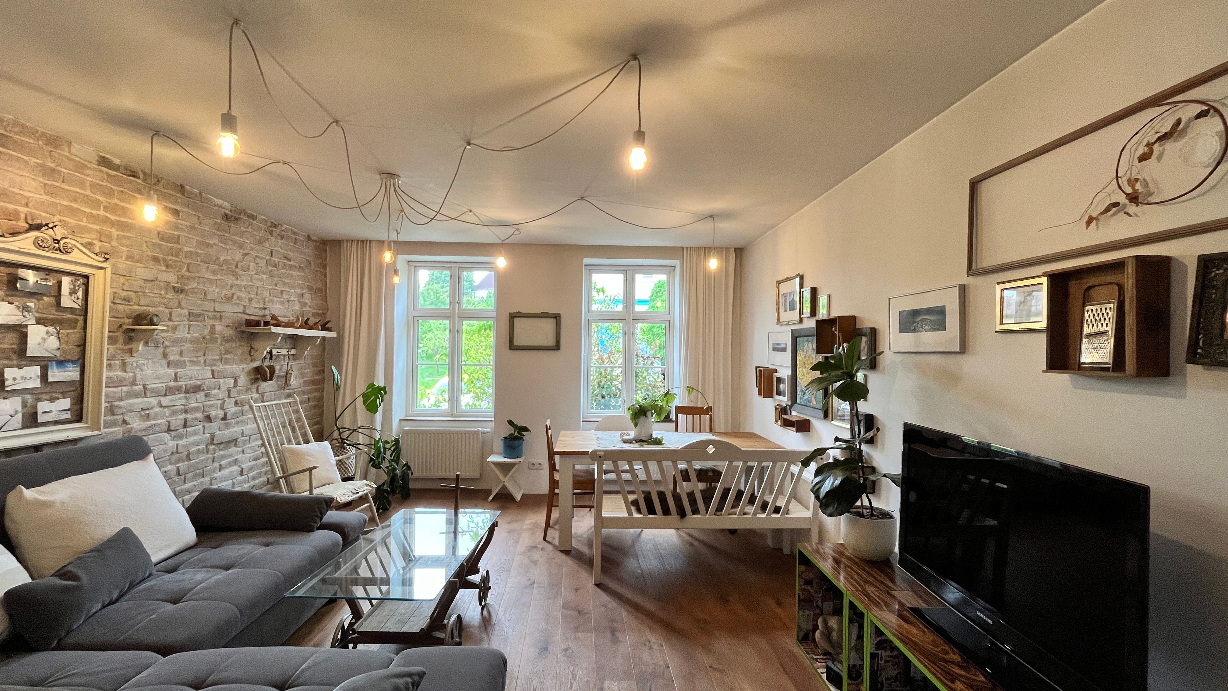 Gemütliches Wohnzimmer mit grauem Sofa, Holztisch, Pflanzen und Wanddekorationen.