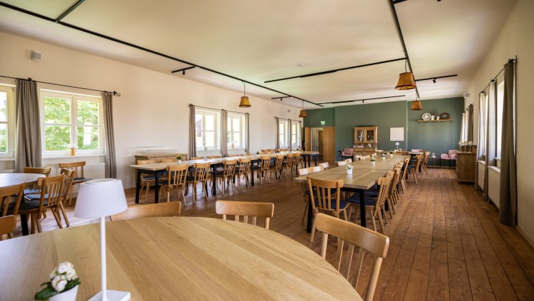 Ein gro&szlig;er, heller Saal mit Holzb&ouml;den und Holztischen und -st&uuml;hlen. Fenster an der linken Wand lassen Tageslicht herein. Der Saal ist modern gestaltet, eine Wand gr&uuml;n gestrichen, der Rest wei&szlig;.